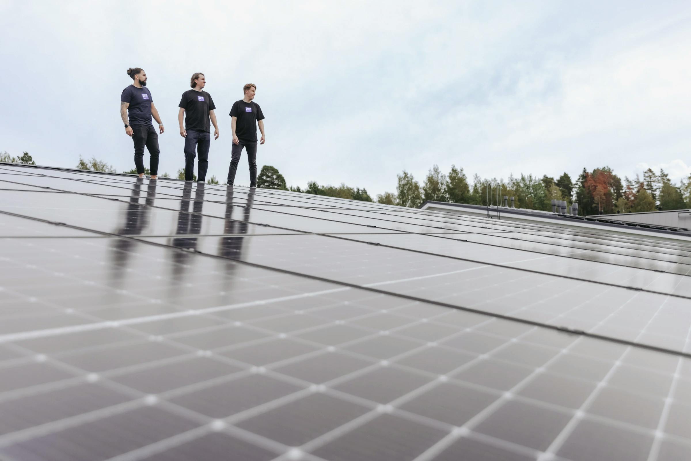 Kolme yrittäjää katolla aurinkopaneeleiden takana